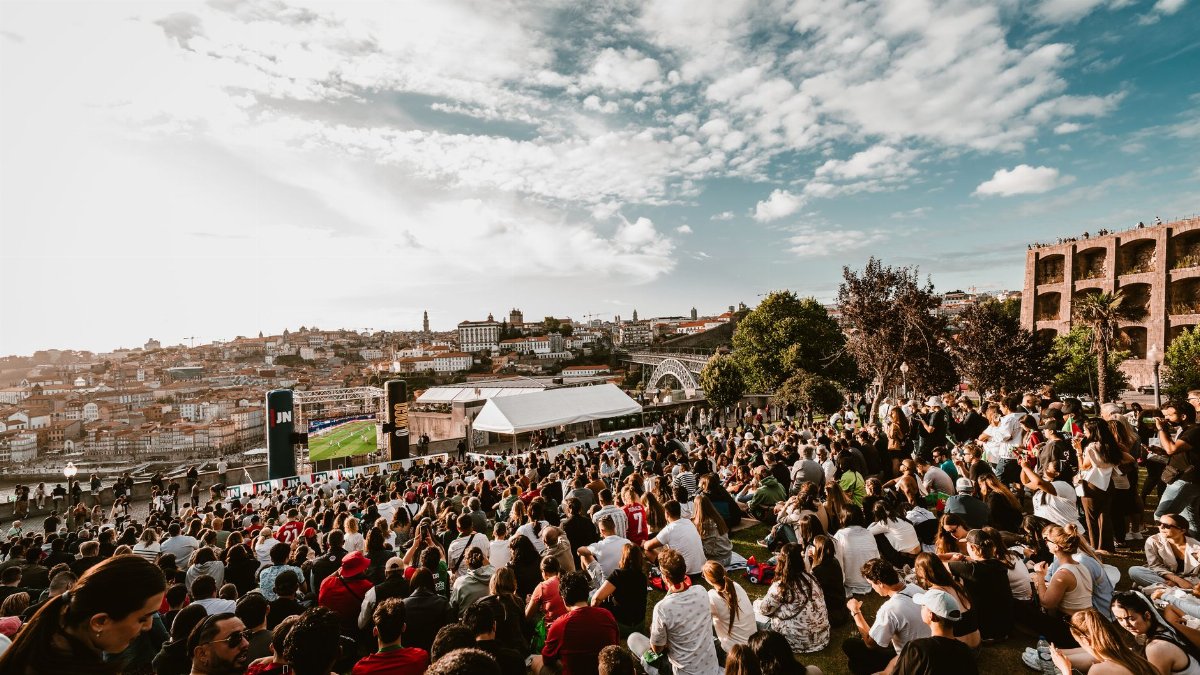 A large crowd gathers in Porto, Portugal, watching a soccer match with the cityscape as a backdrop.