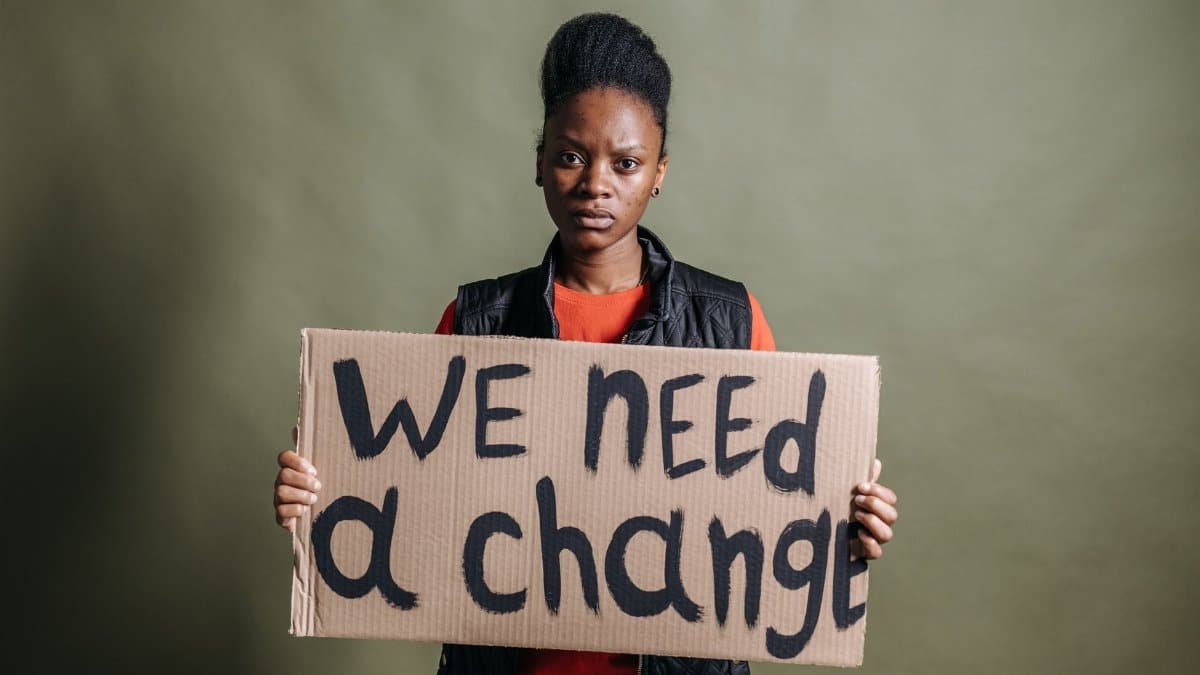 Portrait of an activist with a placard stating 'We need a change', highlighting human rights.