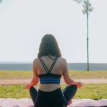 A woman practicing meditation on a yoga mat in a sunny park setting.
