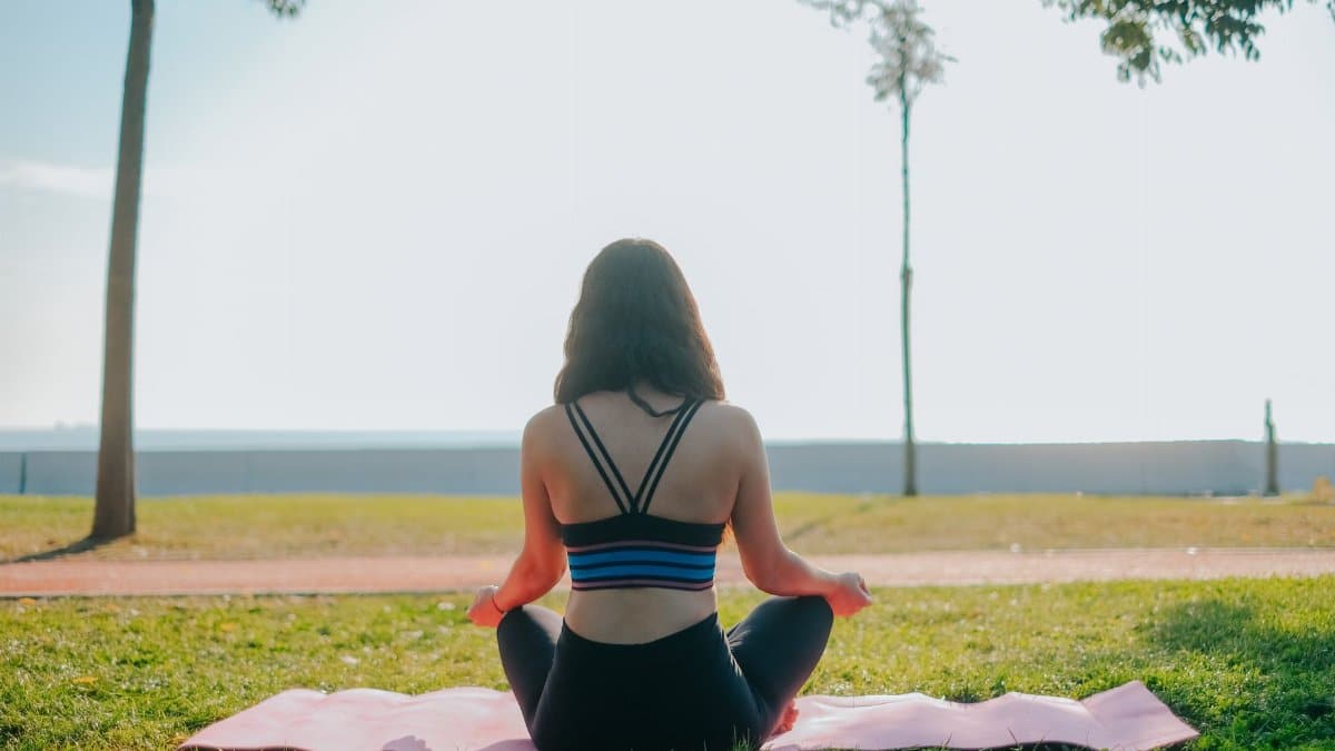 A woman practicing meditation on a yoga mat in a sunny park setting.