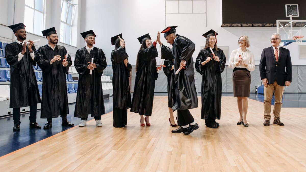 Students and faculty celebrating graduation with high fives in a sports hall.