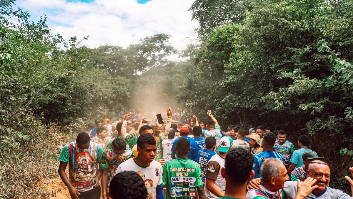 A vibrant crowd walking on a dusty road through the forest during a festival in Barbalha, Brazil.