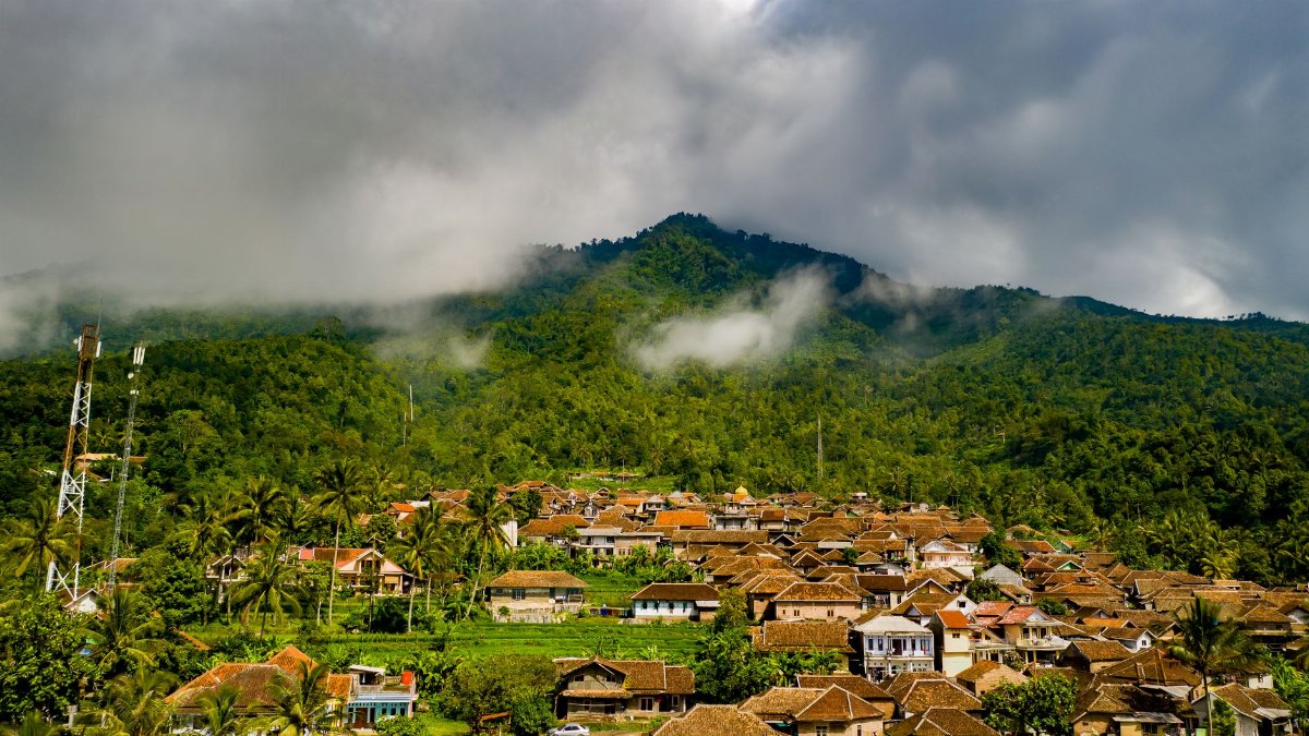 Picturesque rural village in Majasari, Banten surrounded by lush tropical mountains under dramatic cloudy skies.
