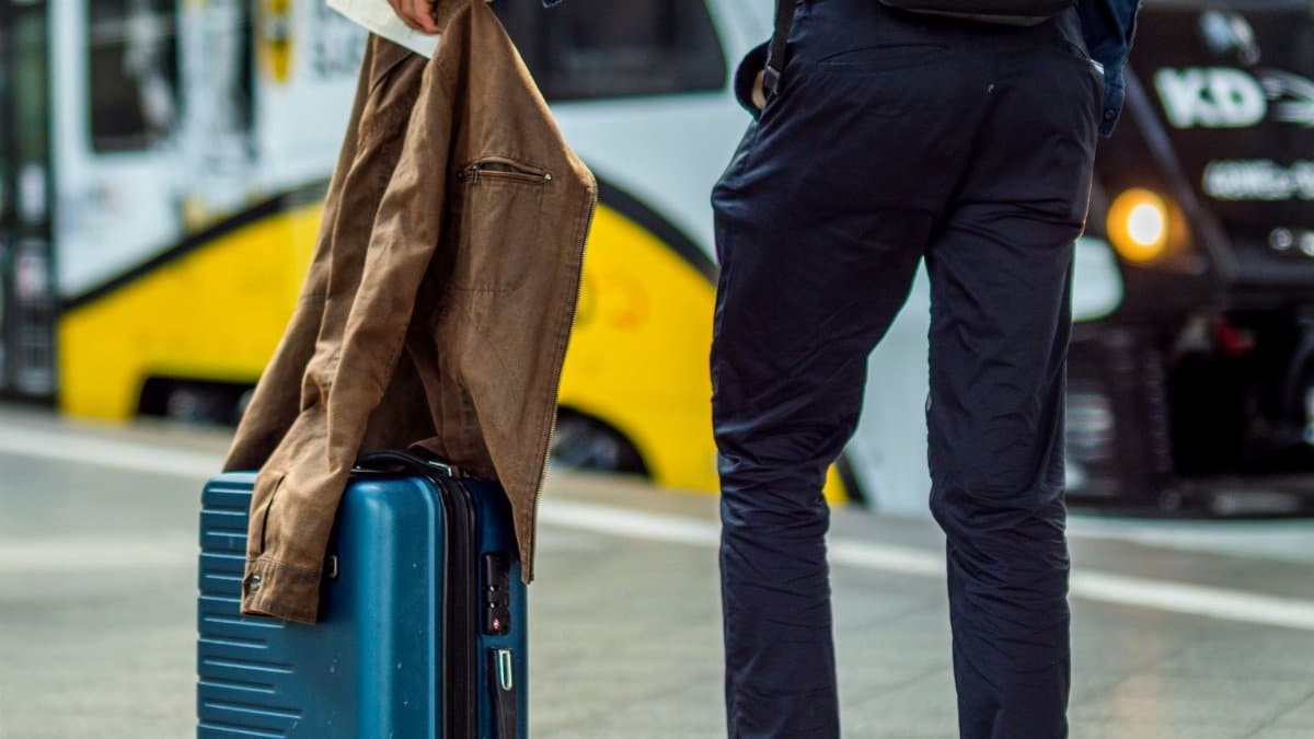Traveler with suitcase waiting at train station platform.