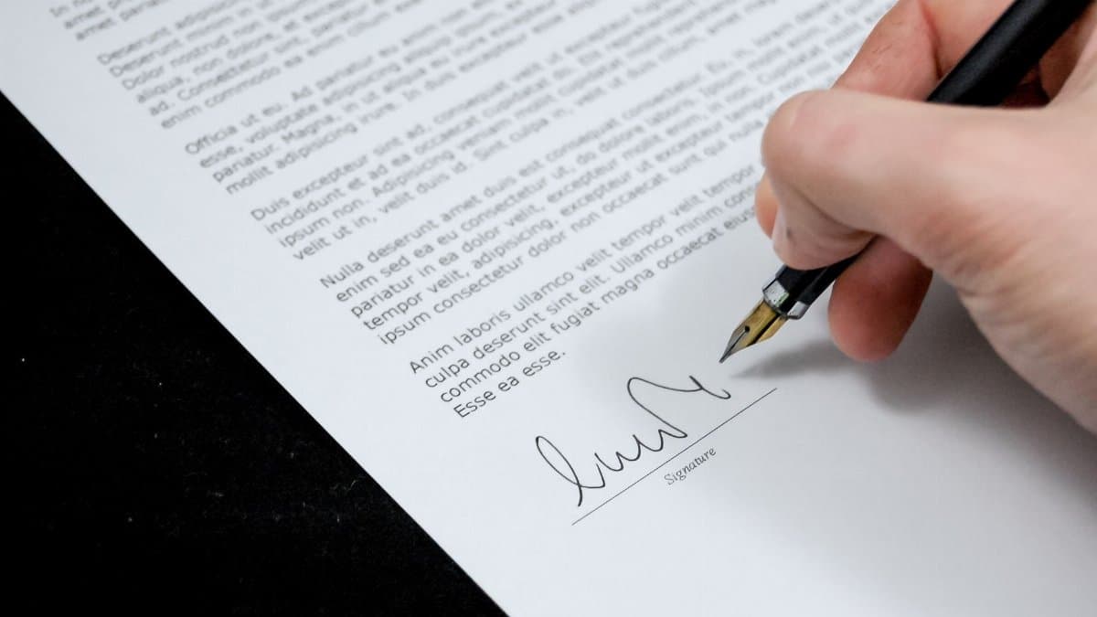 Close-up of a hand signing a formal document with a fountain pen, indicating agreement.