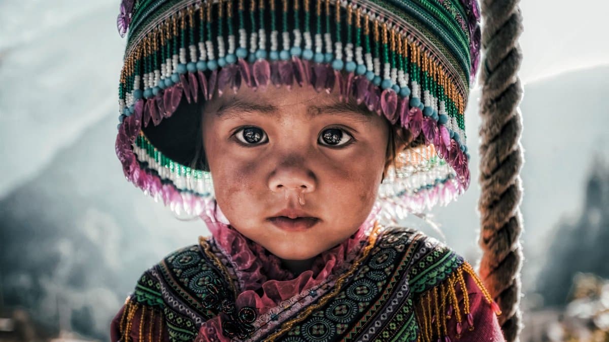 Close-up of a Vietnamese child in traditional attire with a colorful hat, highlighting cultural heritage.