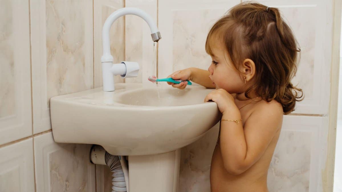 A young child with brown hair brushes teeth using a toothbrush by the sink, showcasing daily hygiene habits.