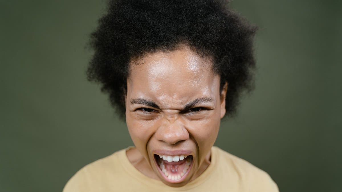 Close-up of an African American woman with afro hair expressing anger in a studio setting.
