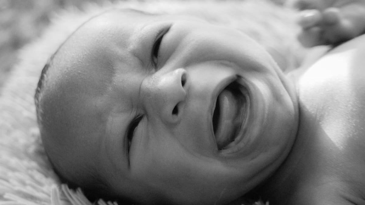 Emotive black and white close-up of a crying newborn baby with strong emotional expression.