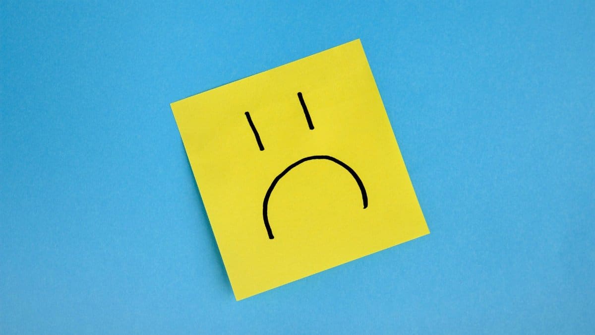 Yellow sticky note with sad face doodle on blue background, conveying emotions.