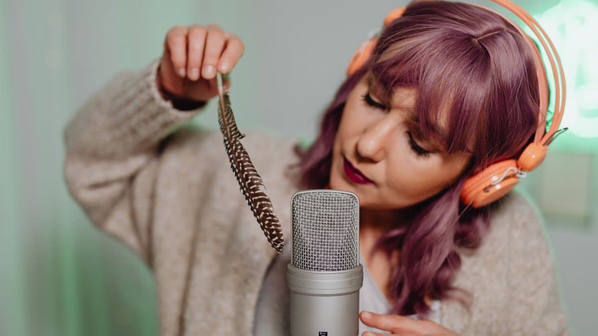 A woman uses a feather and microphone for ASMR recording in a cozy home studio.