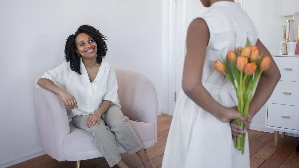 A touching Mother's Day celebration as a daughter surprises her mother with a bouquet of tulips indoors.
