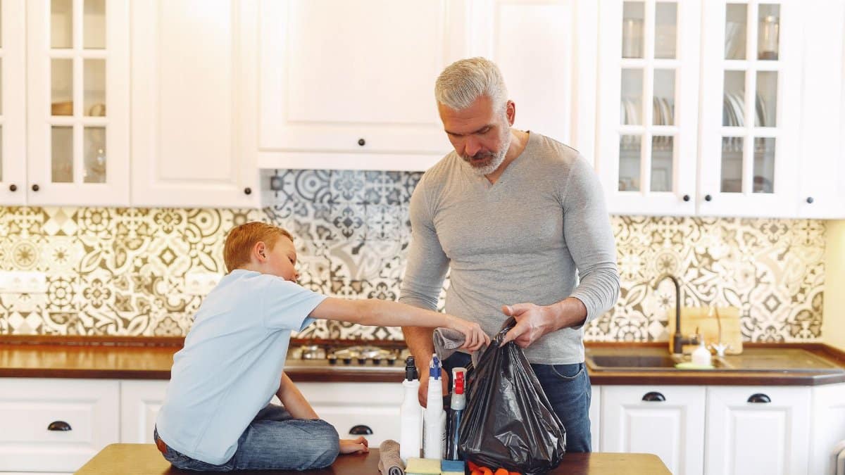 Grey haired dad with beard and small kid preparing cleaning stuff for tidying up kitchen