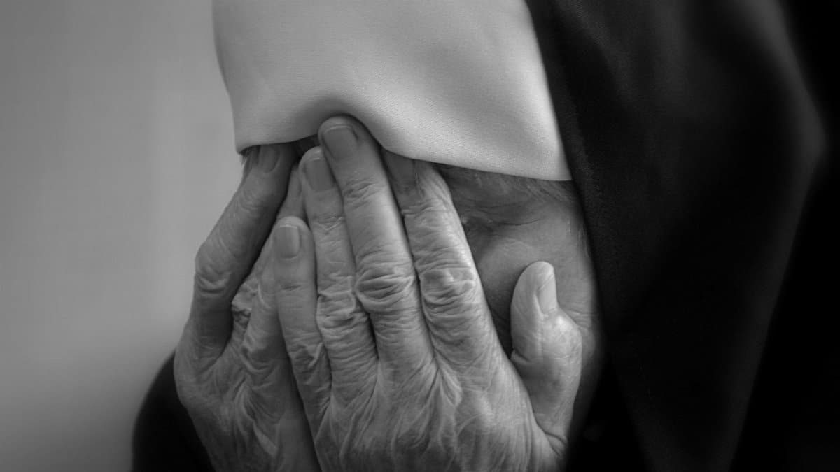 A poignant black and white portrait showing a nun's hands covering her face in grief, reflecting sorrow and mourning.