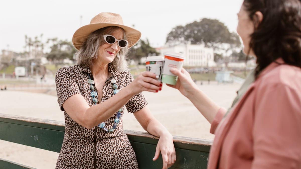 Two women enjoying a day outdoors, toasting with coffee in a sunny setting.