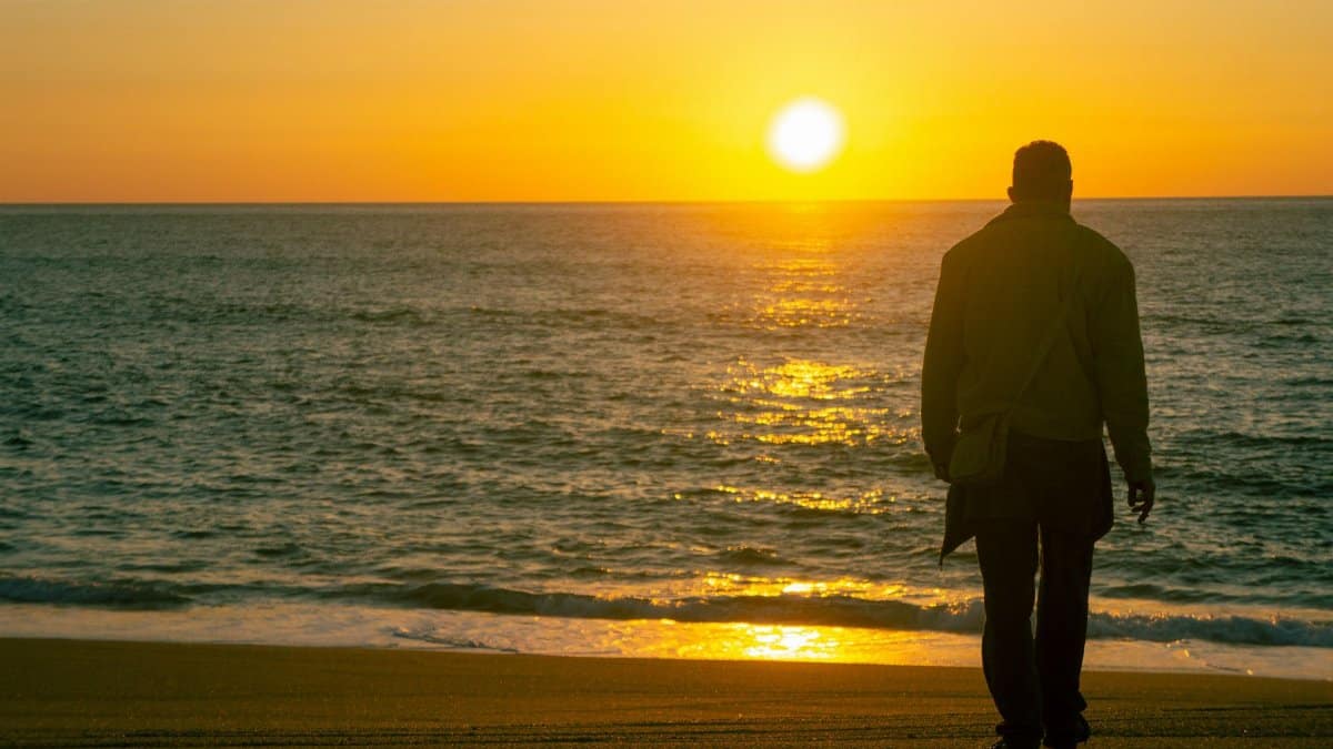 A man enjoys a tranquil sunset on a sandy beach in Porto, Portugal.