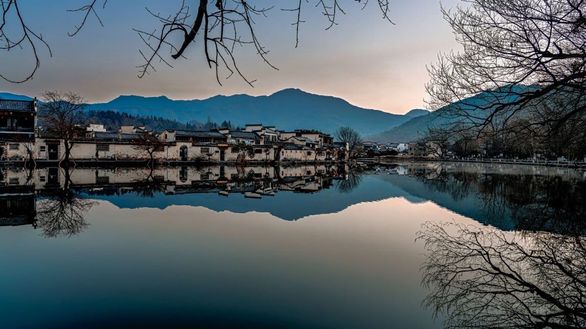 Scenic view of a serene lake reflecting mountain village at dusk.