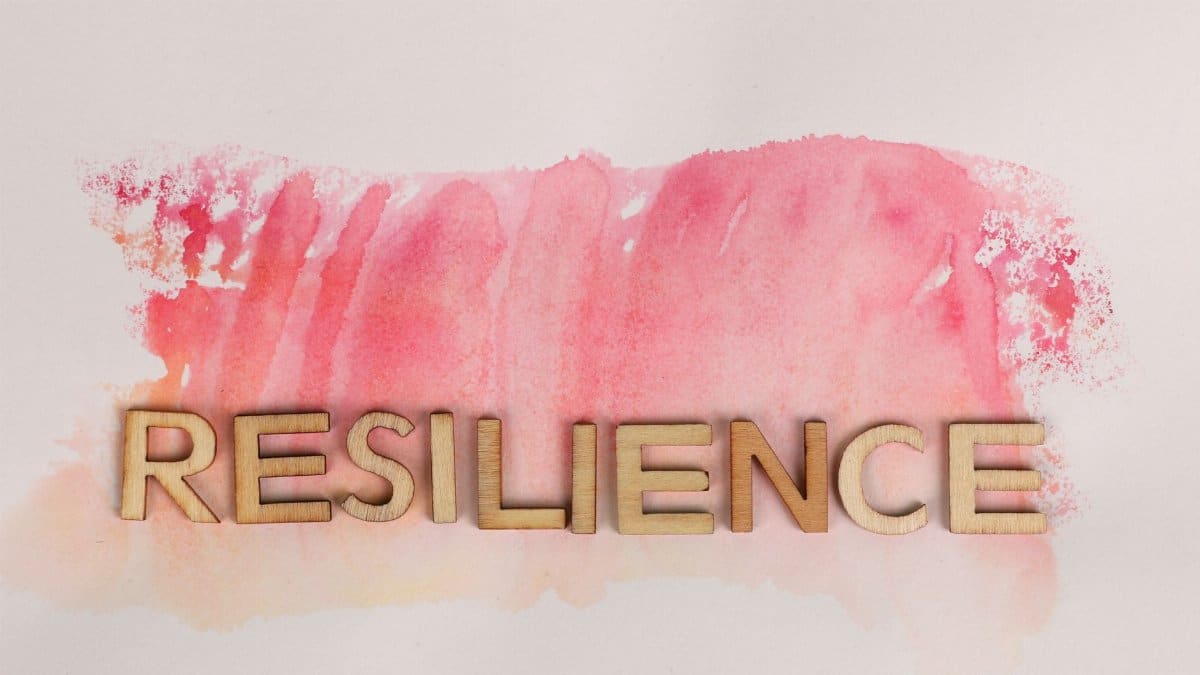 Wooden letters spelling 'resilience' on pink watercolor background, creative typography.