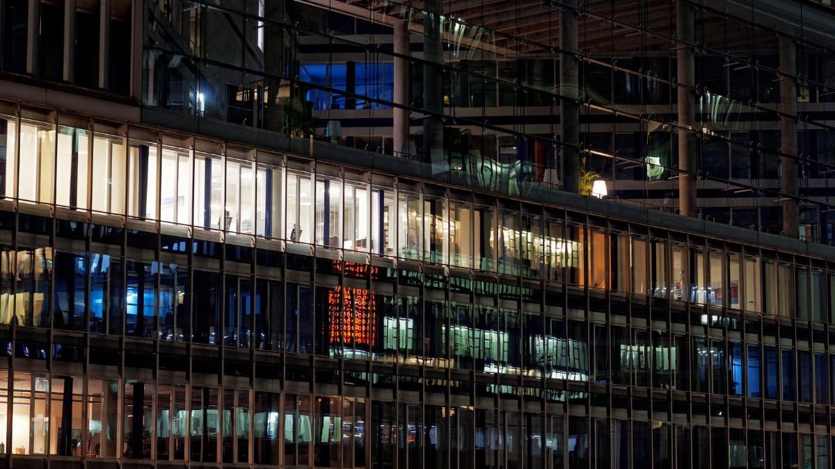 A modern glass building at night, showcasing illuminated windows and reflections.
