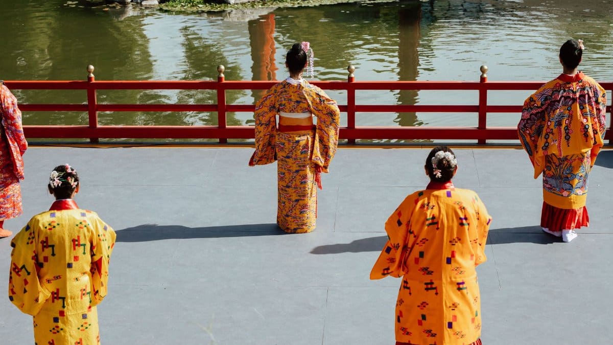 Japanese women in vibrant kimonos performing a cultural dance by a serene pond.
