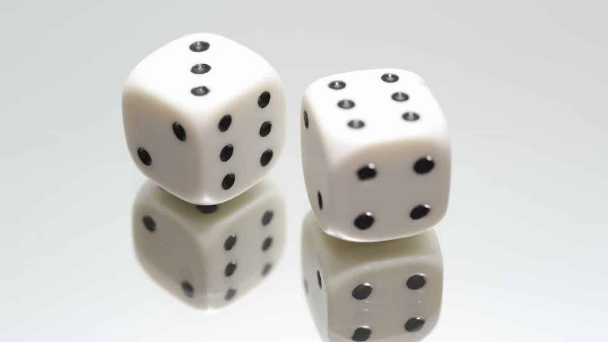 A close-up view of two white dice with reflection on a smooth white surface, symbolizing luck and chance.