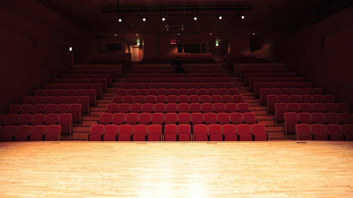 An empty theater interior with rows of red seats and an illuminated stage.