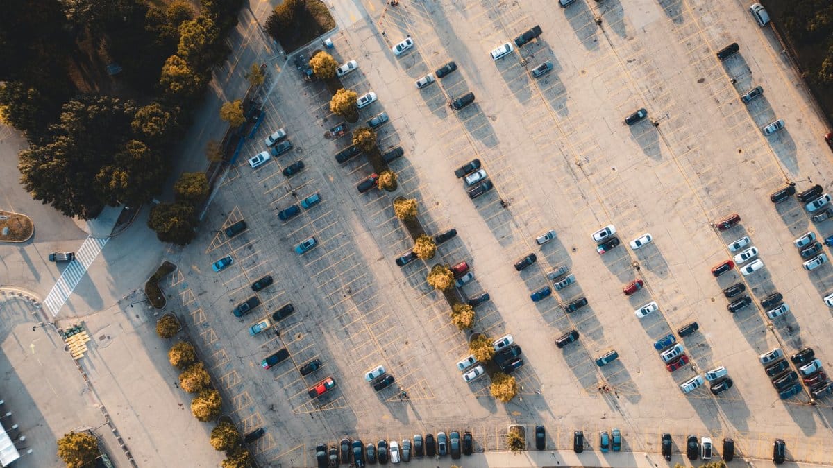 Top-down aerial shot of a parking lot with scattered cars and surrounding trees.