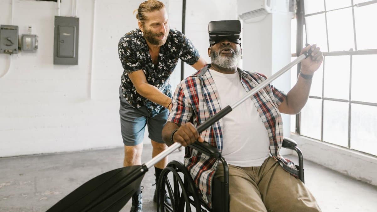 Two men enjoying virtual reality; one is in a wheelchair experiencing a rowing simulation.