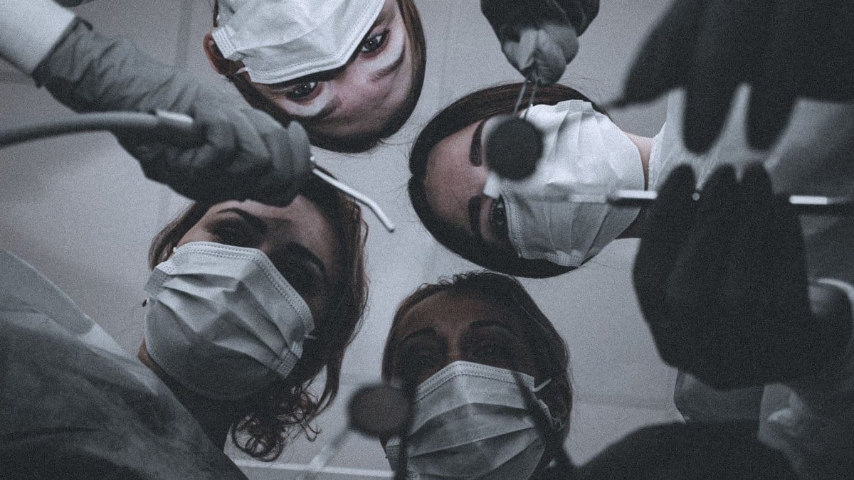 A team of dentists wearing masks and gloves, viewed from below, holding dental tools.