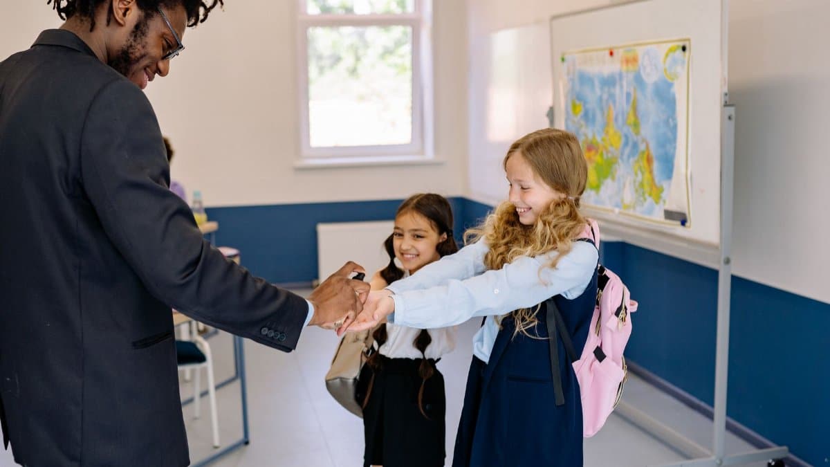 A teacher sanitizing two young students' hands in a classroom setting, promoting hygiene.