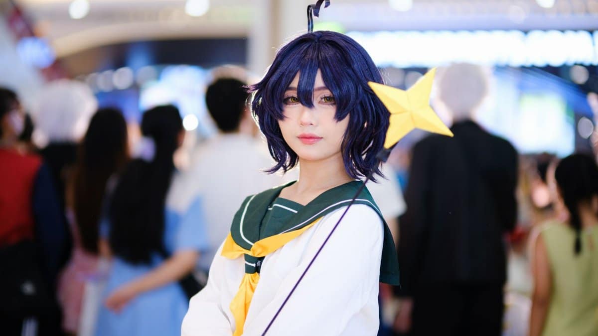Cosplayer dressed as anime character with a star wand at a bustling indoor event.