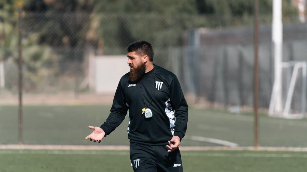 Football coach directing young players during training session on a sunny day.