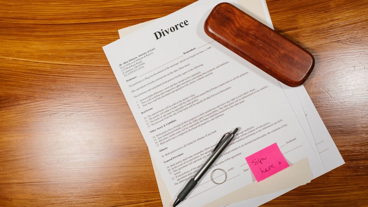 Flat lay of divorce papers with a pen and ring on a wooden table for legal themes.