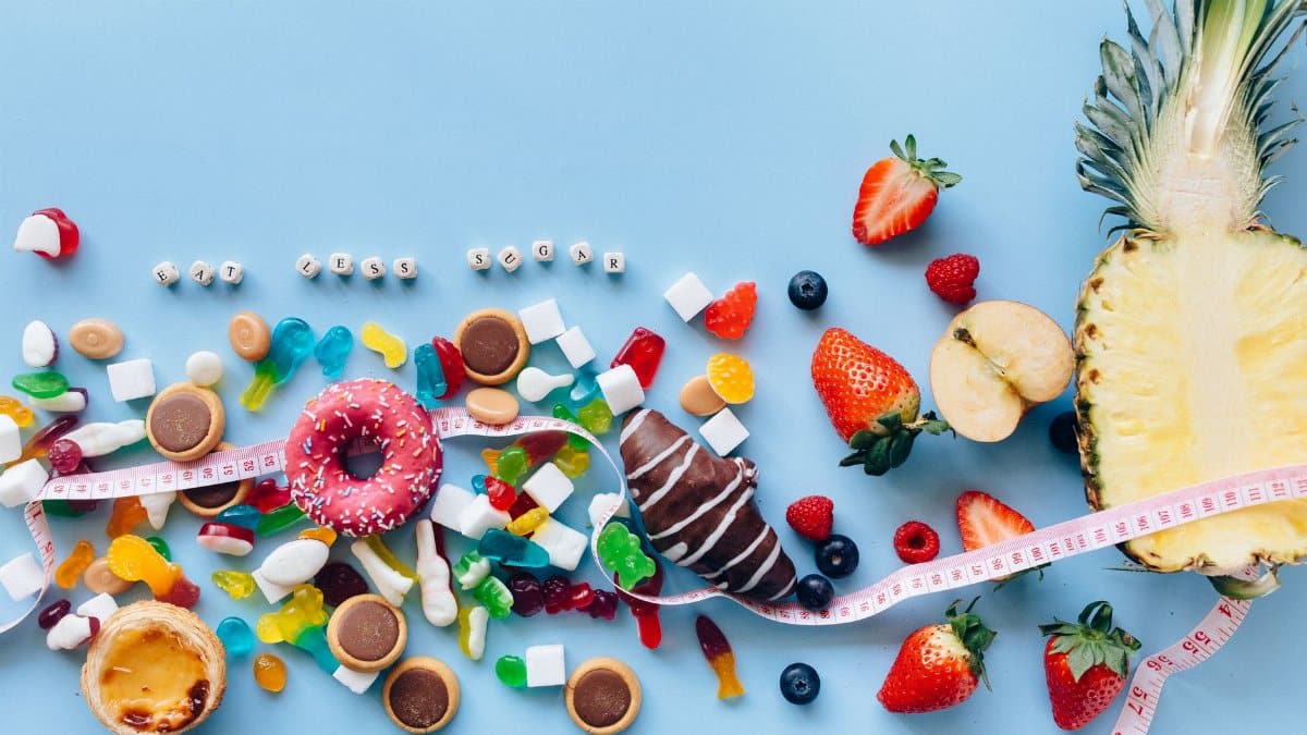 Flat lay of sweets and fruits on blue background with health message 'Eat Less Sugar'.