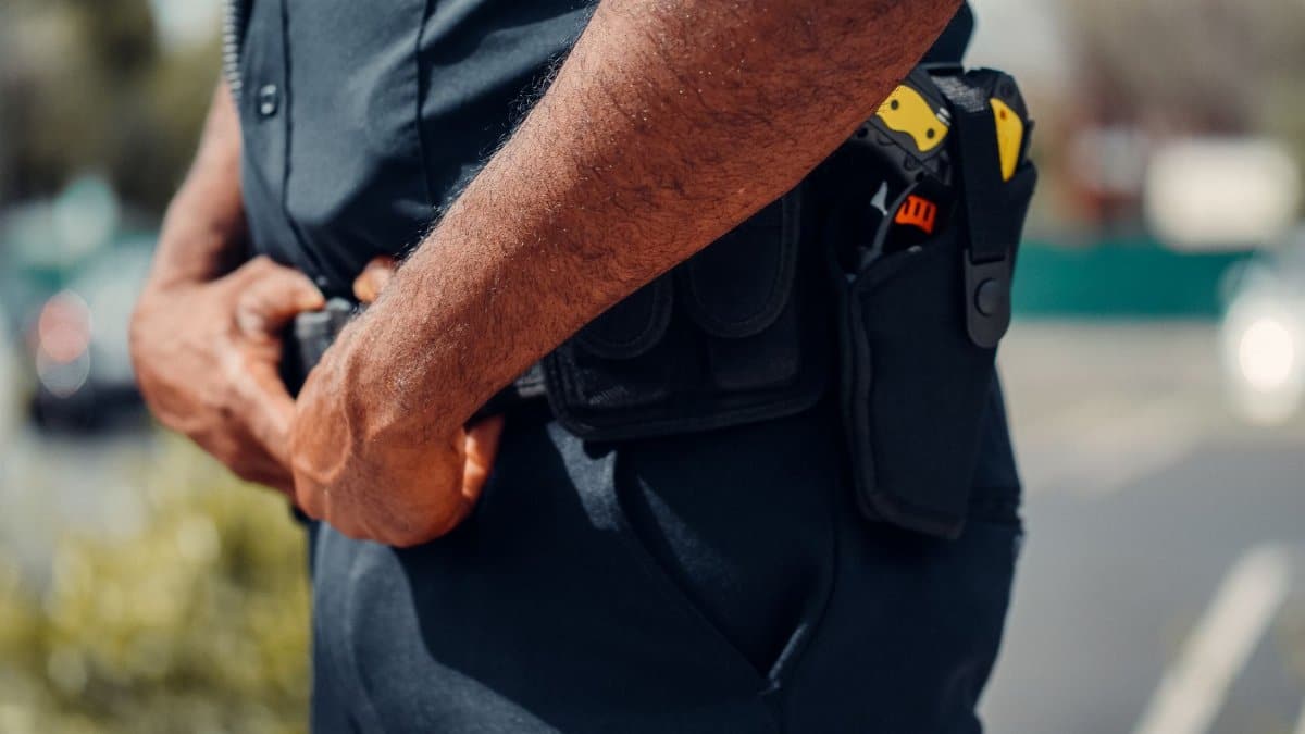 A close-up view of a police officer's uniform and equipment. Focus on belt and hands.