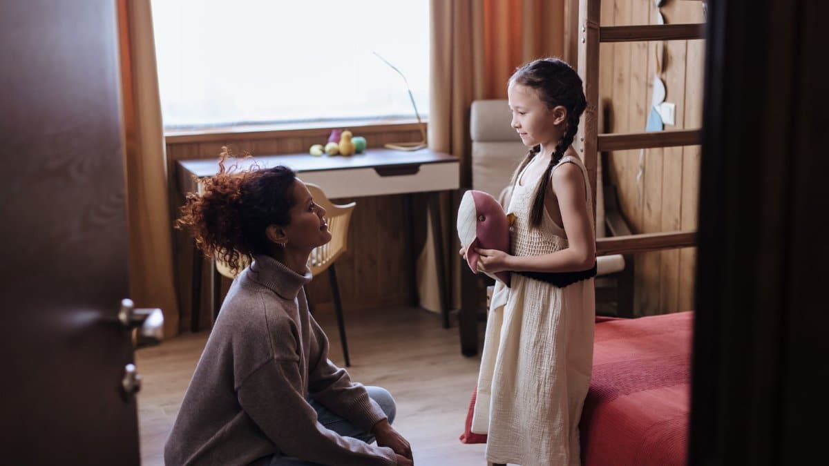 Mother kneeling and talking to her daughter in a cozy home interior, fostering a loving family bond.