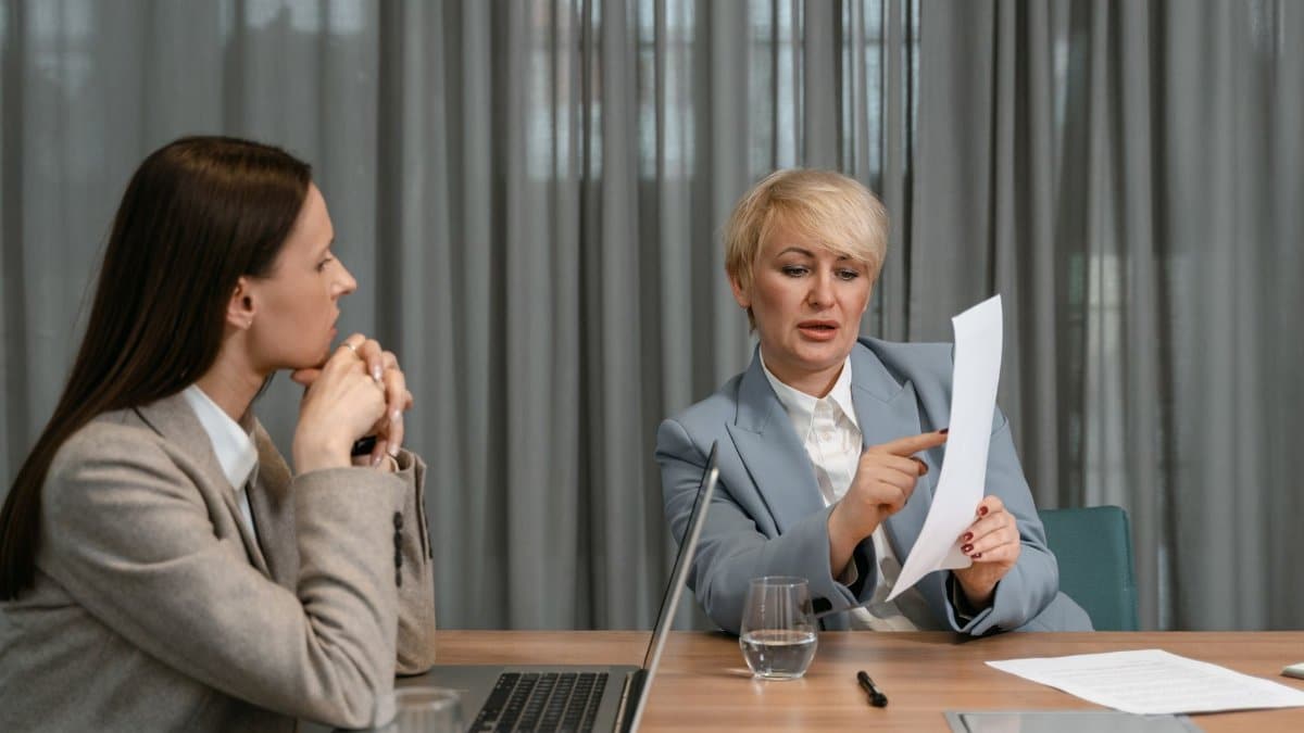 Two businesswomen discussing documents during a professional meeting around a conference table.