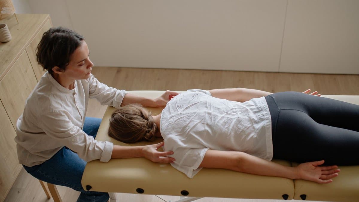 A therapist performs a chiropractic adjustment on a woman lying on a treatment table indoors.