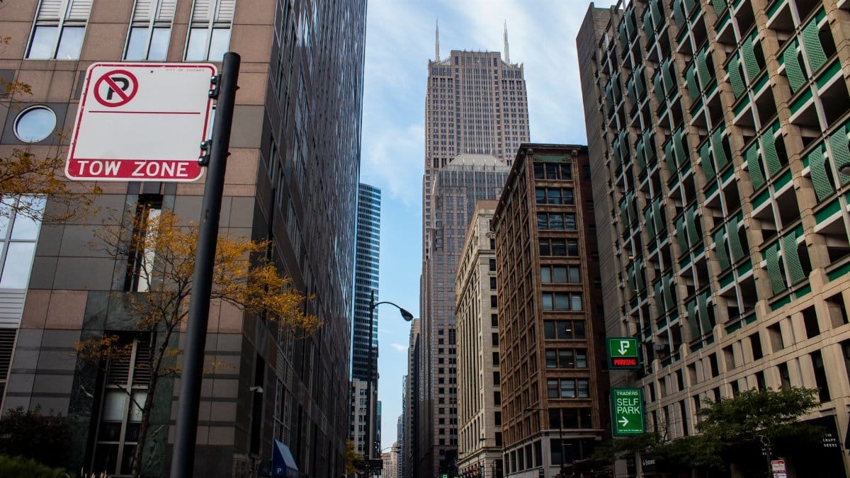 View of a busy urban street in Chicago with skyscrapers and a prominent tow zone sign.