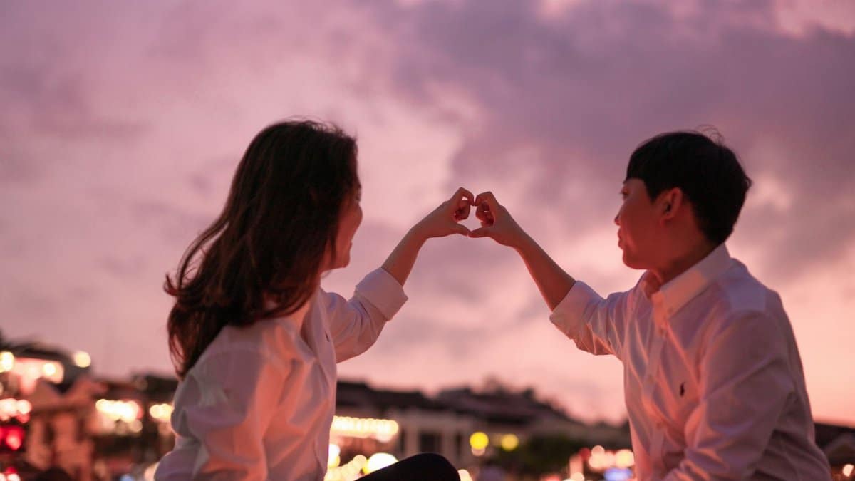 Romantic couple creating a heart with hands during a beautiful sunset.