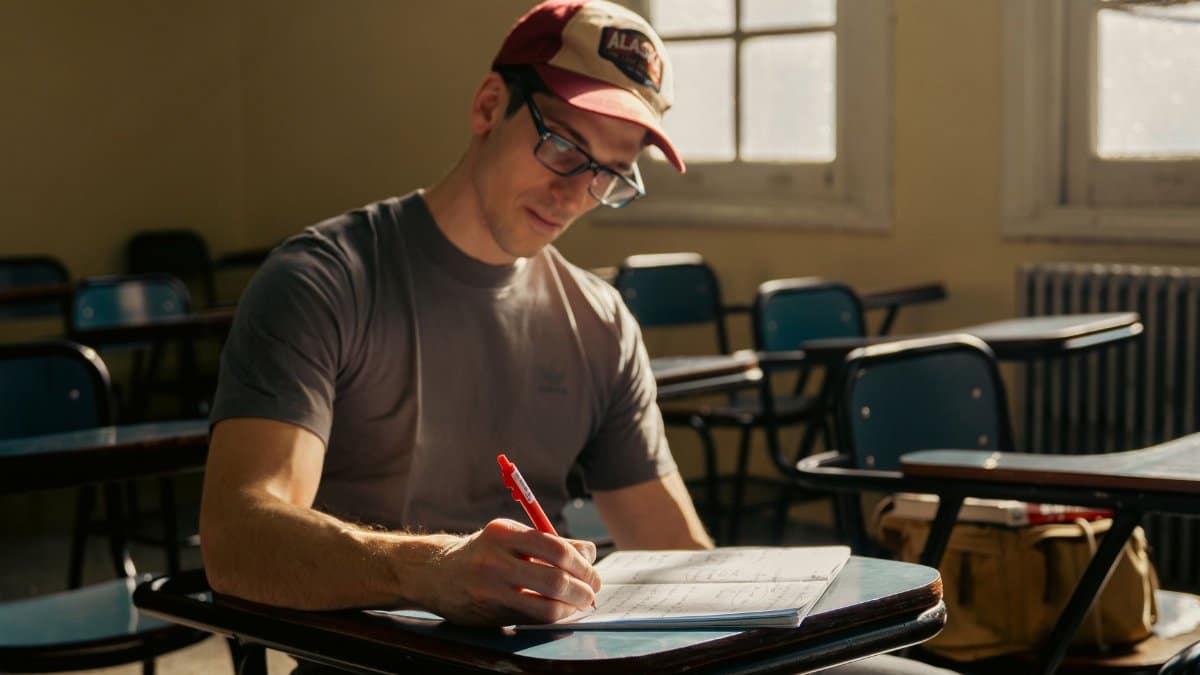 Adult male student studying at a university classroom desk during the day.