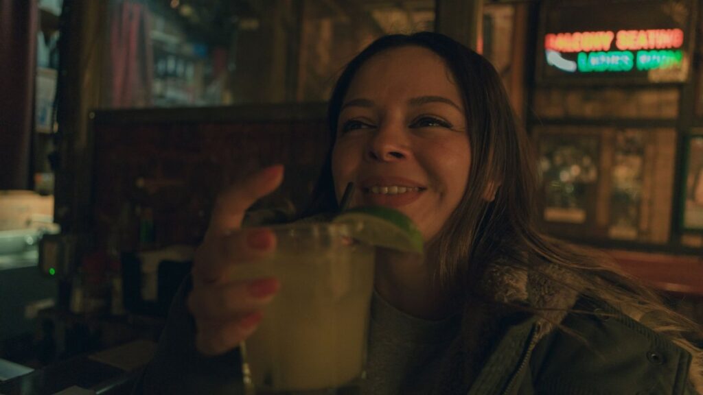 A cheerful woman savoring a cocktail in a cozy San Francisco bar, embracing the night ambiance.