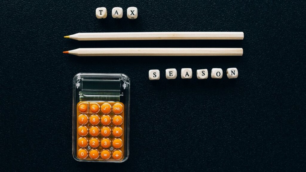 Top view of pencils, calculator, and letter blocks spelling 'tax season' on black background.