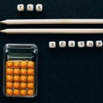 Top view of pencils, calculator, and letter blocks spelling 'tax season' on black background.