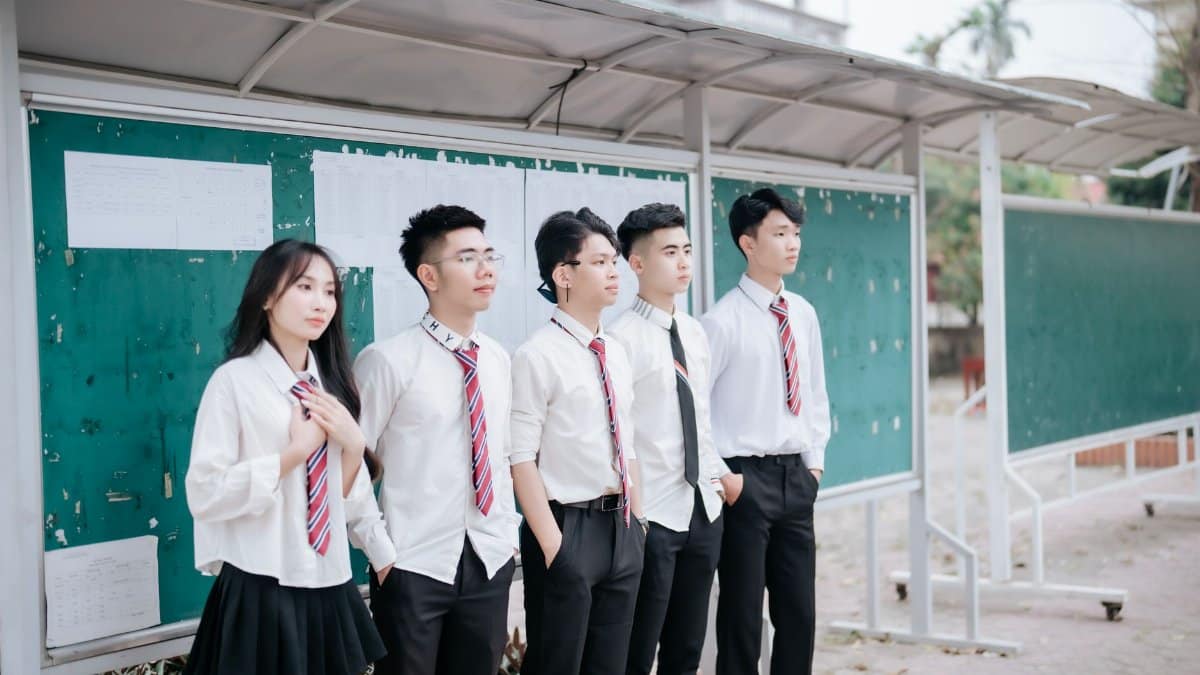 A group of students in uniform standing by the school bulletin board outdoors.
