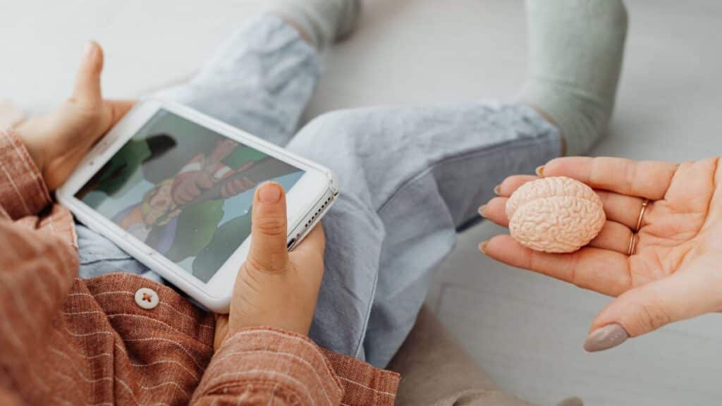 A child watches a cartoon on a tablet as an adult holds a brain model.