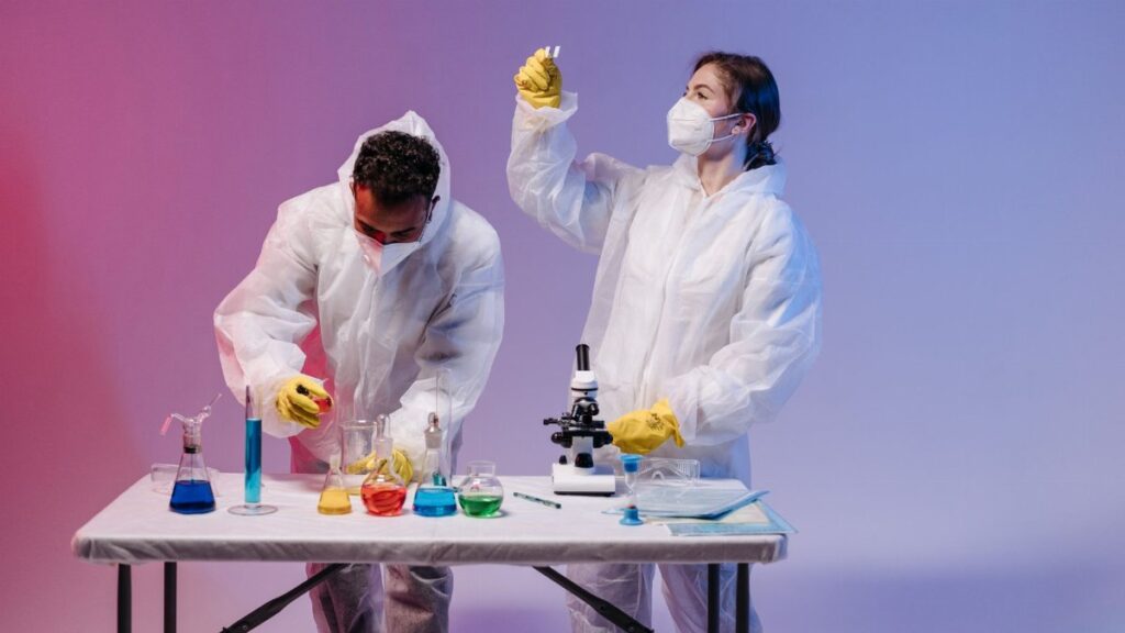 Two scientists in protective gear conducting experiments with colorful chemicals in a lab.