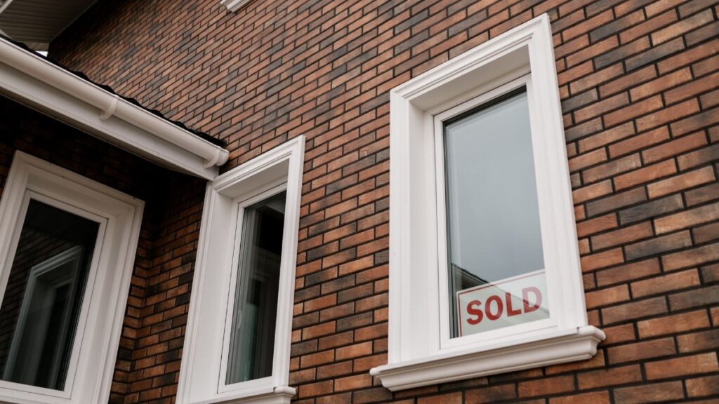 Close-up of a brick house with a 'Sold' sign in the window, showcasing real estate sales.