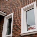 Close-up of a brick house with a 'Sold' sign in the window, showcasing real estate sales.