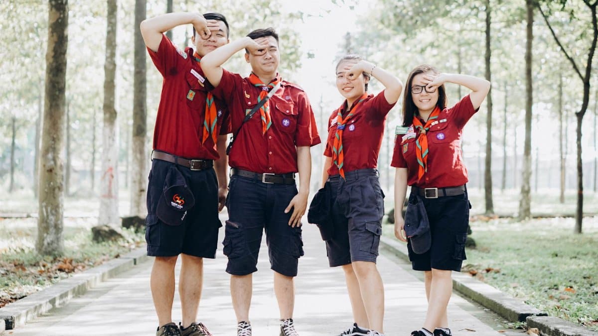 Four young scouts in uniform salute confidently while standing on a sunny pathway.